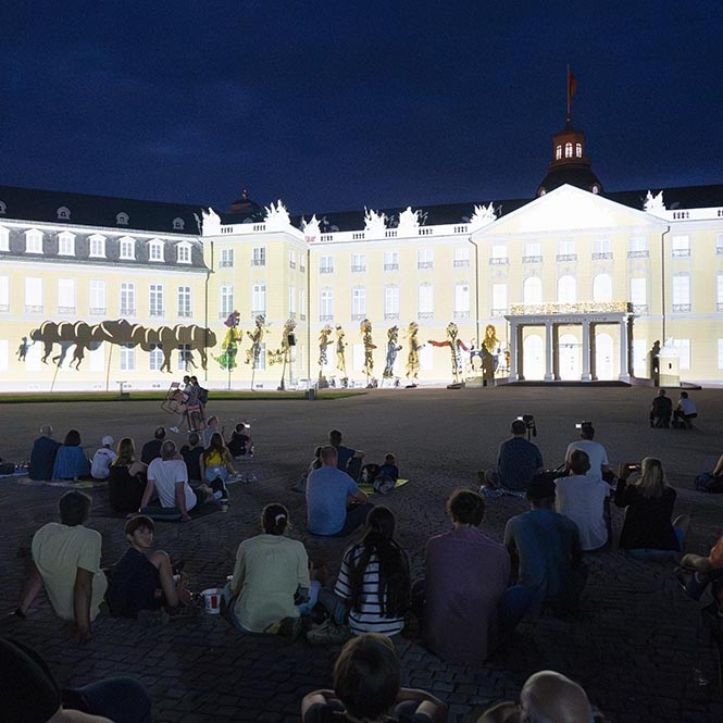 Die vordere Fassade des Karlsruher Schlosses bei Nacht. Ein Film der Schlosslichtspiele wird auf die Fassade projiziert. 