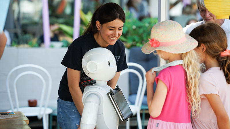 Drei Personen, davon zwei Mädchen, interagieren mit einem Roboter.